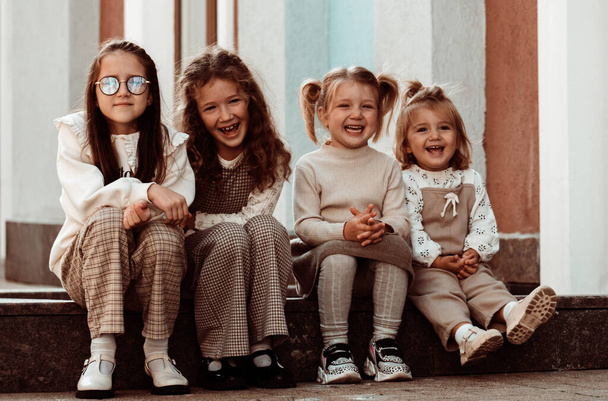 Retrato al aire libre de cuatro hermanas sentadas en la calle.Lindos modelos en ropa beige. - Foto, imagen