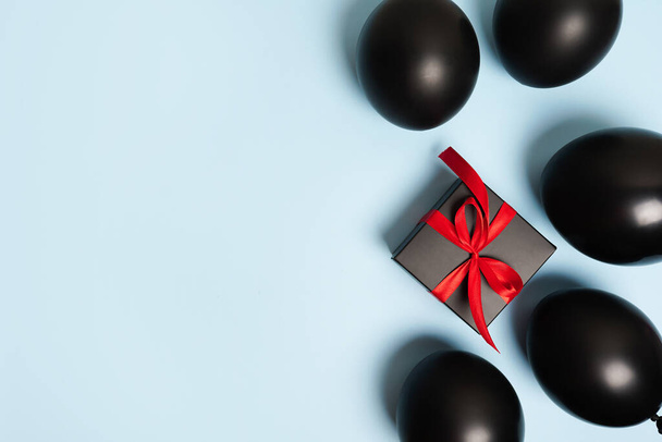 Caja de regalo envuelta en papel negro con cinta roja sobre fondo azul. Vista superior con espacio de copia. - Foto, Imagen