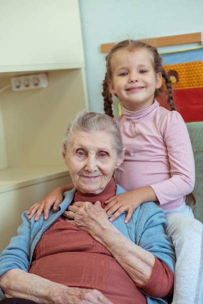 Ritratto di una vecchia e di una bambina, nonna abbraccia la nipote, legami familiari, vecchiaia e giovinezza, 90 anni, rughe su un viso vecchio, bella vecchiaia, una donna e un bambino. - Foto, immagini