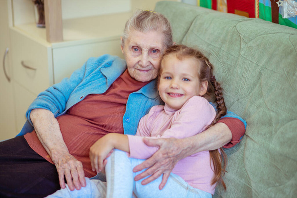 Portret van een oude vrouw en een klein meisje, oma knuffelt haar kleindochter, familiebanden, ouderdom en jeugd, 90 jaar, rimpels op een oud gezicht, mooie ouderdom, een vrouw en een kind. - Foto, afbeelding