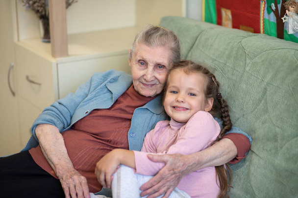 Retrato de una anciana y una niña, abuela abraza a su nieta, lazos familiares, vejez y juventud, 90 años, arrugas en una cara vieja, hermosa vejez, una mujer y un niño. - Foto, Imagen