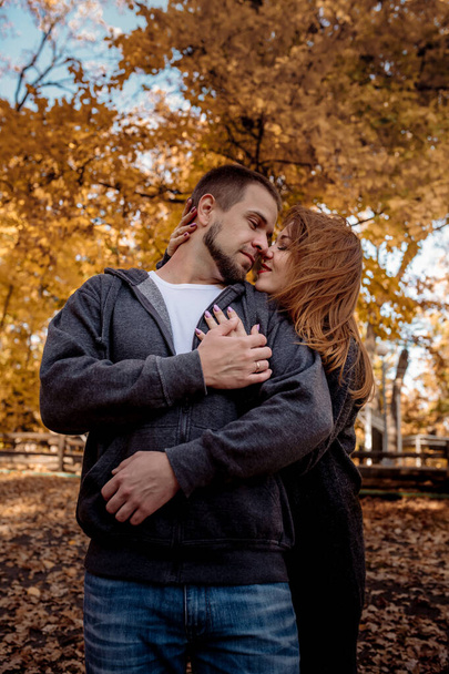 Beautiful young couple man and woman hugging in the park near the pond in leaf fall in autumn - Φωτογραφία, εικόνα
