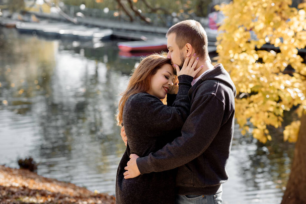 Beautiful young couple man and woman hugging in the park near the pond in leaf fall in autumn - Photo, Image