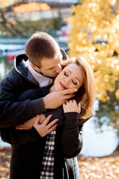 Beautiful young couple man and woman hugging in the park near the pond in leaf fall in autumn - Φωτογραφία, εικόνα