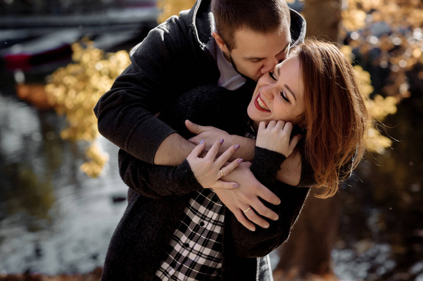 Beautiful young couple man and woman hugging in the park near the pond in leaf fall in autumn - Фото, зображення