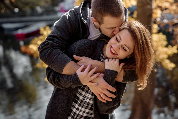Beautiful young couple man and woman hugging in the park near the pond in leaf fall in autumn - Foto, imagen