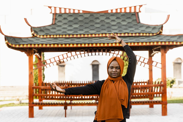 Qigong chinese meditation and sport training outdoor. Black muslim woman is meditating outdoor near chinese arbor - Photo, Image