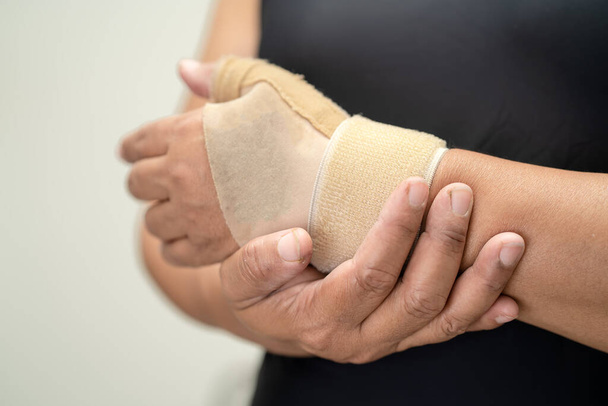 Азиатская женщина среднего возраста использует эластичный бинт для лечения синдрома Де Квербена под рукой и пальцем в офисе
. - Фото, изображение