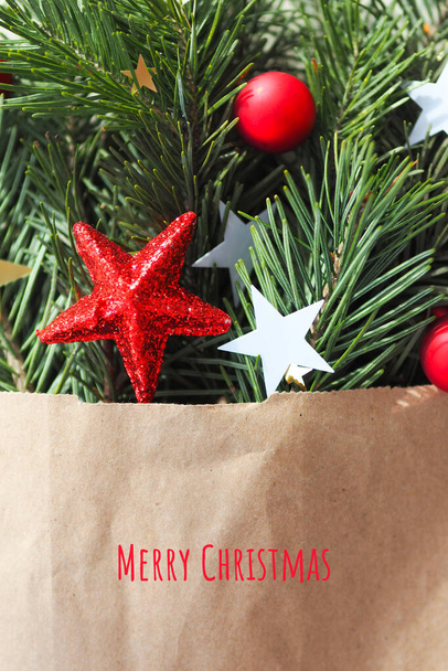 Χριστουγεννιάτικη κάρτα με την επιγραφή Καλά Χριστούγεννα. βιοτεχνία τσάντα και έλατο κλαδιά με κόκκινα και λευκά αστέρια και μπάλες Χριστούγεννα. - Φωτογραφία, εικόνα