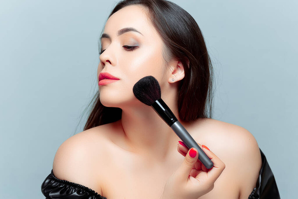 a beautiful young brunette is applying tonal powder with a makeup brush on her face - Foto, Imagen