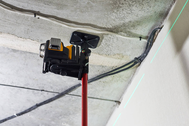 建設現場で壁に見える緑のレーザービームとレーザーレベル測定ツール。測定レベル。ストレッチ天井を設置するための専門機器。家の改装の概念を閉じる - 写真・画像