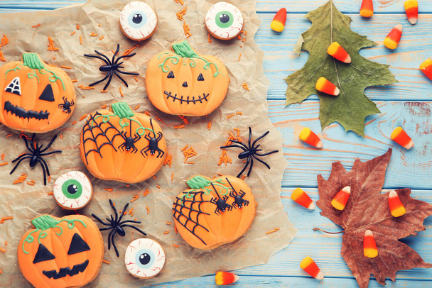 Halloween gingerbread cookies with candies, spiders and dry leafs on blue wooden table - Фото, изображение