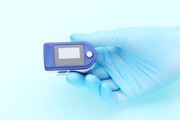Pulse oximeter in doctor hand with glove on blue background - Foto, afbeelding