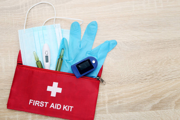 EHBO-kit met pulsoximeter, medicijnmaskers, handschoenen, thermometer en ampullen op bruine achtergrond - Foto, afbeelding
