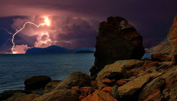 黒海沿岸上空の雷光/コクテベル近くの黒海の岩の多い海岸上空の雷光。曇り空に雲がある。雷は水に反射する。素晴らしい力と自然のエネルギー、要素。ファンタジー風  - 写真・画像