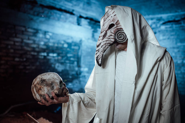 a man dressed as a plague doctor holds a human skull in his hand. costume party for Halloween. cosplay of the horseman of the apocalypse. props burning skull - Photo, Image