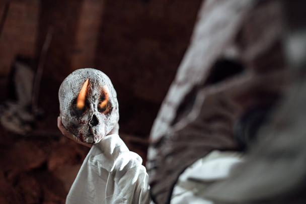 Egy járványügyi orvosnak öltözött férfi egy emberi koponyát tart a kezében. jelmezbál Halloweenkor. Az apokalipszis lovasának cosplay-je. támasztók égő koponya - Fotó, kép