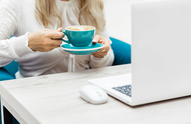  Młoda bizneswoman przy użyciu białego laptopa i picia kawy w pomieszczeniach. - Zdjęcie, obraz