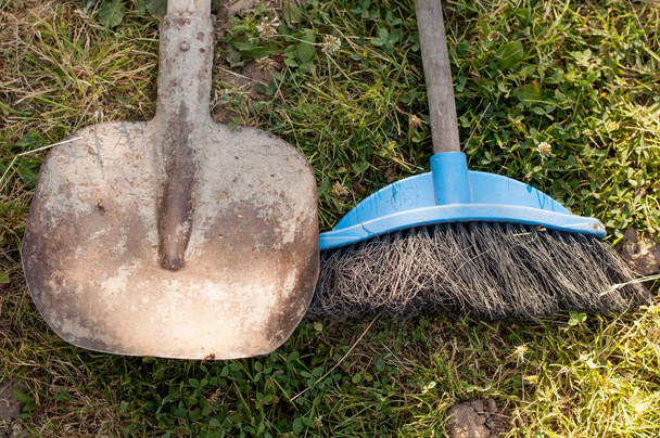 A rusty shovel and a cleaning brush with a blue base lie on the green grass - Foto, imagen