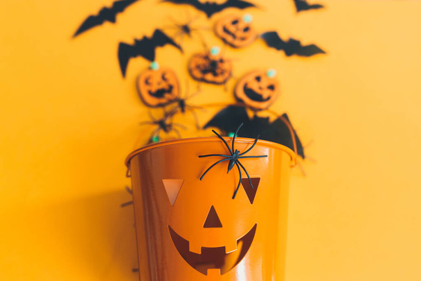Fijne Halloween. Jack o lantaarn emmer met spinnen, vleermuizen en pompoenen op oranje achtergrond bovenaanzicht. Snoep of ik schiet. Halloween decoraties op geel papier - Foto, afbeelding