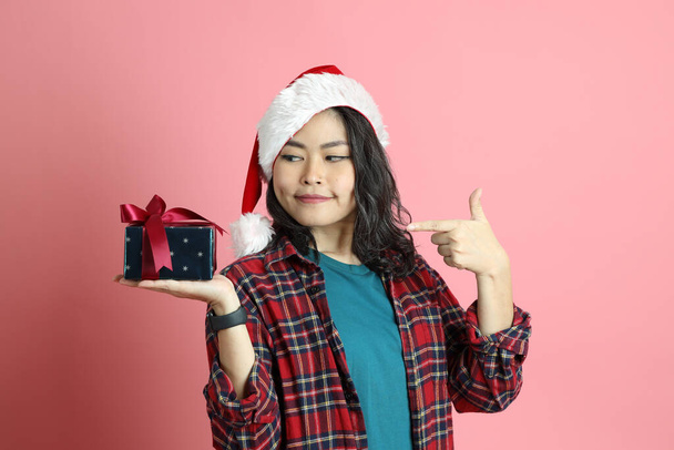The Asian woman with santa hat standing on the pink background. - Photo, image