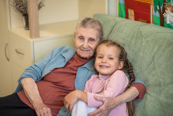 Retrato de una anciana y una niña, abuela abraza a su nieta, lazos familiares, vejez y juventud, 90 años, arrugas en una cara vieja, hermosa vejez, una mujer y un niño. - Foto, Imagen