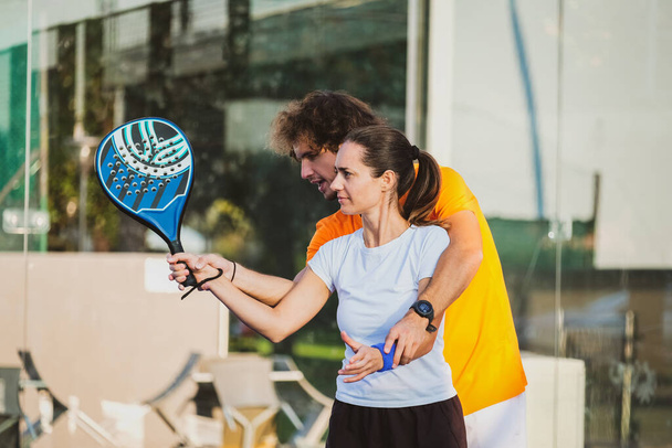 Young teacher is monitoring teaching padel lesson to his student - Coach teaches girl how to play padel on the outdoor tennis court - Φωτογραφία, εικόνα