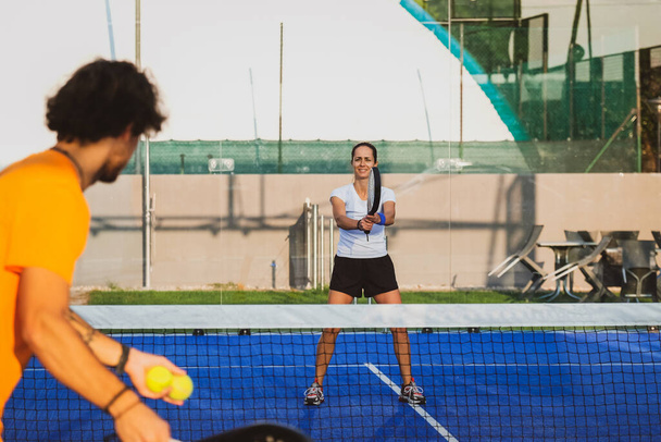 Νεαρός δάσκαλος παρακολουθεί τη διδασκαλία του μαθήματος padel στο μαθητή του - Coach διδάσκει κορίτσι πώς να παίξει padel στο υπαίθριο γήπεδο τένις - Φωτογραφία, εικόνα