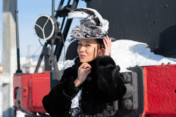 chica vestida como una mujer noble del siglo 19 cerca de una locomotora de vapor. Invierno ruso - Foto, imagen
