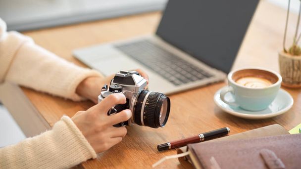Primer plano, Hermosa fotógrafa freelancer milenaria en el escritorio con su cámara retro vintage. - Foto, Imagen