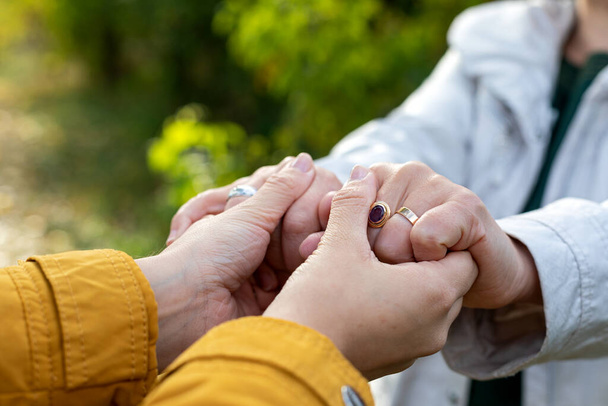Close up picture of mother and daughter holding hands outdoor, autumnal background - Фото, изображение