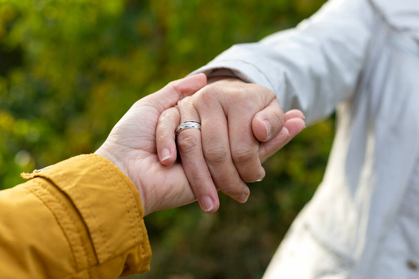 Close up picture of mother and daughter holding hands outdoor, autumnal background - Foto, afbeelding