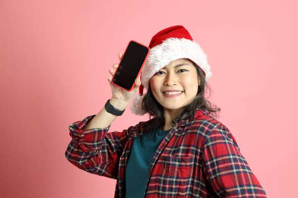 Pembe arka planda duran Noel Baba şapkalı Asyalı kadın.. - Fotoğraf, Görsel