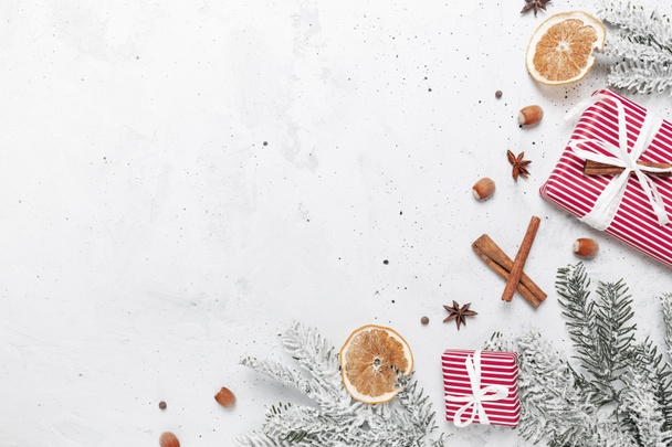 Christmas flat lay top view on white gray concrete background table with present red gift box, decorations, fahéj rúd, mogyoró, szárított narancs szeletek, különböző fűszerek, fenyő, ánizs, ánizs - Fotó, kép
