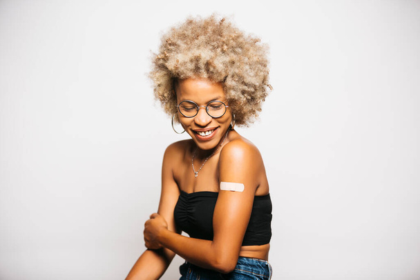 予防接種後に腕にバンドエイドを見せる若い黒人ラテン系女性の肖像背景 - 写真・画像