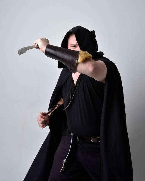  portrait of red haired man wearing medieval viking inspired fantasy costume with dark cloak. Standing pose  with gestural hand movements as if casting a spell, isolated  against studio background. - Photo, Image