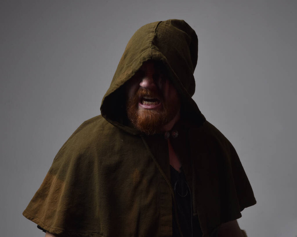  Portret rudego mężczyzny ubranego w średniowieczny kostium wikinga inspirowany fantastycznym płaszczem z ciemnymi cieniami i farbą do twarzy. na ciemnym tle studio z oświetleniem sylwetki. - Zdjęcie, obraz