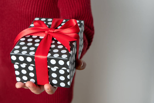 Mujer sosteniendo un regalo en su mano. Un lazo rojo. Fondo gris. Navidad o San Valentín. Vista frontal, espacio para copiar - Foto, imagen
