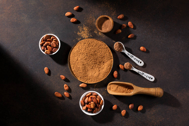 Schalen mit Bio-Kakaopulver und aromatischen rohen Kakaobohnen auf dunklem rustikalem Holzgrund. Draufsicht, Kopierraum, flache Lage. Super-Brain-Food-Konzept. - Foto, Bild