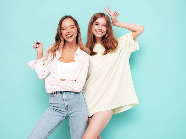 Two young beautiful smiling brunette hipster female in trendy summer clothes. Sexy carefree women posing near blue wall. Positive models having fun. Cheerful and happy  - Photo, image