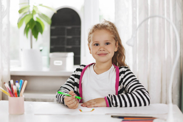 Portret uroczej dziewczyny, która rysuje tęczę w albumie z kolorowymi ołówkami. Praca domowa, szkolenie domowe, odległość społeczna - Zdjęcie, obraz