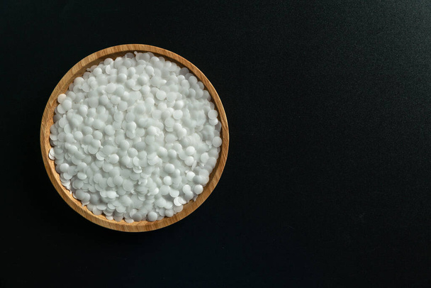 Białe plastikowe koraliki na tle drewna, koraliki polimerowe lub żywica polimerowa, paleta polimerowa, Produkt z zakładów petrochemicznych. polimer granulatu, - Zdjęcie, obraz