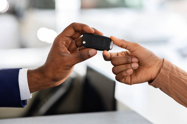 Κοντινό πλάνο του πωλητή αυτοκινήτων δίνοντας τα κλειδιά για το μαύρο θηλυκό πελάτη στο showroom - Φωτογραφία, εικόνα