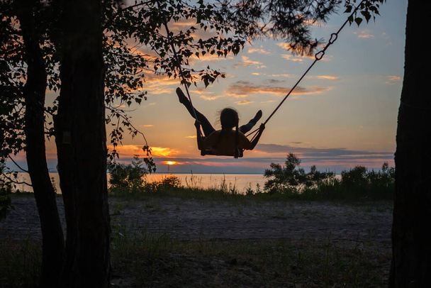 Girl on swing by sea in autumn sunset, family walk in nature, fall vibes, travel, active lifestyle - Photo, Image