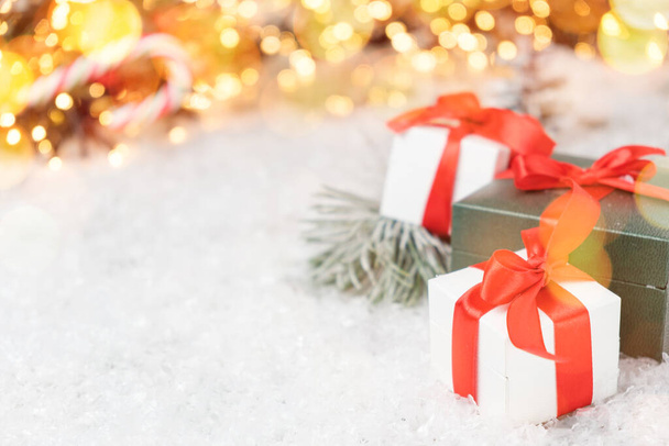 Hermosos regalos de Navidad con rama de pino, nieve y luces bokeh en el fondo con espacio de copia. Tarjeta postal, cupón de descuento o concepto de venta.  - Foto, Imagen