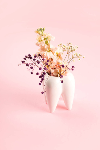 Vaso da dente grande bianco con fiori su sfondo rosa. Estetica dentista da lavoro e ortodontista. - Foto, immagini