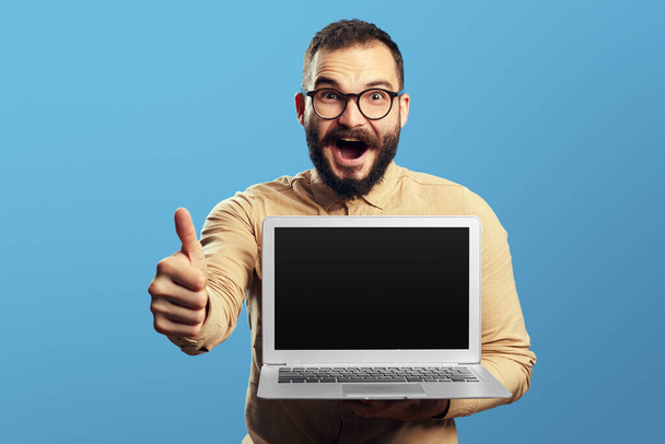 Férfi gazdaság laptop és mutatja üres képernyőn, miközben mutatja hüvelykujját felfelé - Fotó, kép
