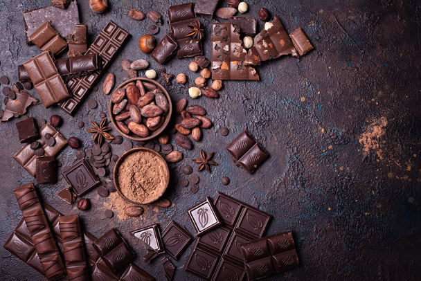 Pieces of broken tasty milk and dark chocolate bars with cocoa beans, hazelnut and powder on black concrete background - Foto, Bild
