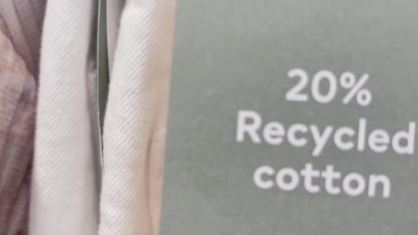 Sustainable fashion and clothing retail concept. 20 percent recycled cotton tag on clothes in mass market apparel brand store in shopping mall - Footage, Video