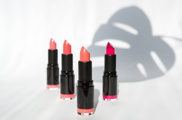 colored bright lipstick of various pink shades on a white background with shadows of leaves and bright lipstick. background for makeup artist. articles and advertising of cosmetics. copy space. - Photo, Image